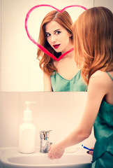 Redhead girl near mirror with heart it in bathroom.
