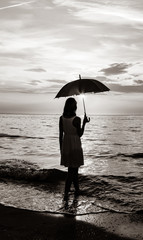 Young beautiful girl on the beach at sunrise with umbrella. Image in black and white style
