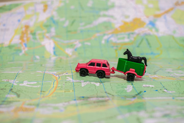 A toy car with a trailer to transport a horse. The pink car is traveling by geographic map. The...