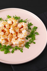 Boiled shrimp and parsley on a pink plate. Macro. The concept of healthy eating. The background is black. Copy space. Vertical shot. Top view.