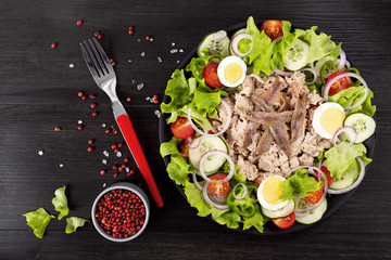 Salad with tuna, anchovies and vegetables. Mediterranean food. The background is black. Top view. Copy space. Horizontal shot.