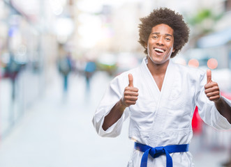 Afro american man wearing karate kimono over isolated background success sign doing positive gesture with hand, thumbs up smiling and happy. Looking at the camera with cheerful expression, winner