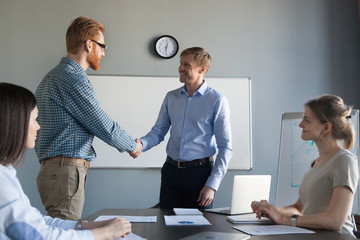 Smiling ceo promoting or rewarding congratulating successful employee with handshake at team...