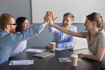 Excited happy business team of employees or partners group giving high five during meeting...