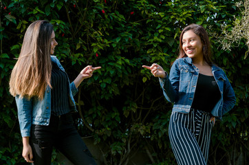 Obraz premium Cheerful friends are gossiping in the park. The girls are pointing with their finger and laughing.