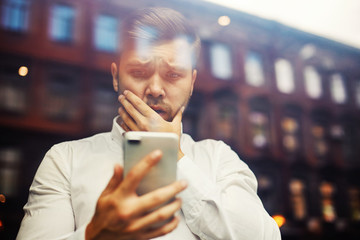 Young shocked businessman watching phone