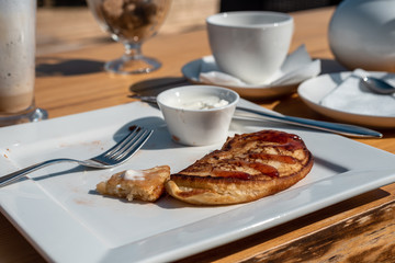 Deadpan image of pancake with honey, sour cream on wooden table with fork, spoon, smartphone and Cup of tea
