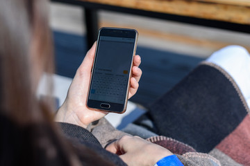 Girl with smartphone in hand from the back on the terrace of a summer cafe, message good morning