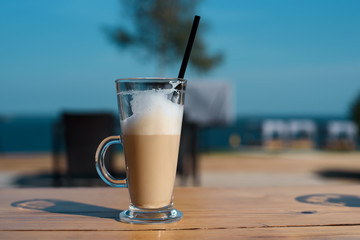 Glass mug with a latte with a tube on a wooden table, with a black straw