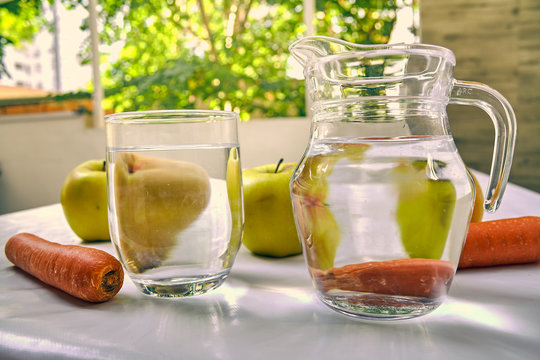 Jug and glass of water with fruits from behind