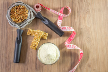 Fitness concept with dumbbells skipping rope measure tape whey protein and bananas on wooden table background.