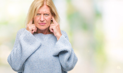 Middle age blonde woman wearing winter sweater over isolated background covering ears with fingers...