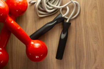 Fitness concept with dumbbells skipping rope measure tape whey protein and bananas on wooden table background.