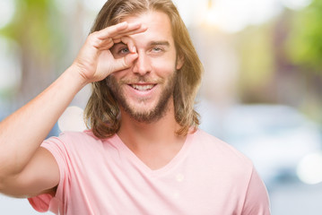 Young handsome man with long hair over isolated background doing ok gesture with hand smiling, eye looking through fingers with happy face.