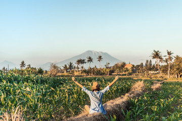 Fototapeta na wymiar Young woman tourist traveler with straw hat on cornfield on a volcano Agung background at sunset time. Bali island. Mount Agung.