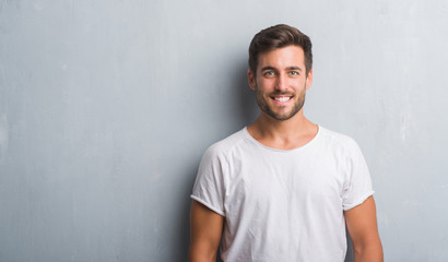 Handsome young man over grey grunge wall with a happy and cool smile on face. Lucky person.