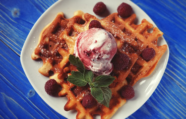 Waffles with raspberry ice cream and fresh raspberries, decorated with mint over blue wooden background