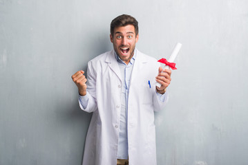 Handsome young doctor man over grey grunge wall holding diploma screaming proud and celebrating...