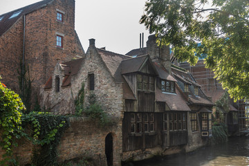 Fototapeta na wymiar Brugge, Flanders, Belgium - September 19, 2018: Brick houses with wooden facades along canals in Bruges offers shades of brown under silver sky with some green foliage.