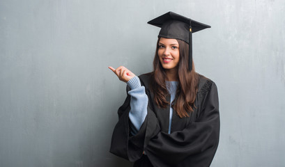 Young brunette woman over grunge grey wall wearing graduate uniform very happy pointing with hand...