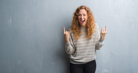 Fototapeta na wymiar Young redhead woman over grey grunge wall shouting with crazy expression doing rock symbol with hands up. Music star. Heavy concept.