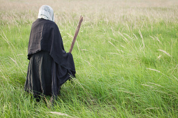 evil old witch hunched over the field among the tall grasses, taking a broom