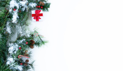 Snow covered Christmas tree branches and decorations on left side of solid white background