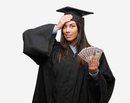 Young hispanic woman wearing graduated uniform holding dollars stressed with hand on head, shocked with shame and surprise face, angry and frustrated. Fear and upset for mistake.