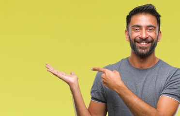 Adult hispanic man over isolated background amazed and smiling to the camera while presenting with hand and pointing with finger.