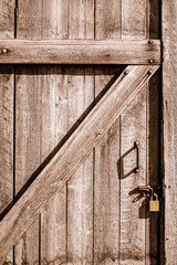 Close-up of wood door to an old house bolted shut with flat gold padlock.