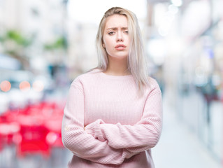 Young blonde woman wearing winter sweater over isolated background skeptic and nervous,...