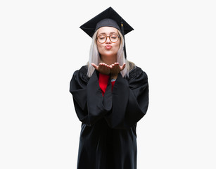 Young blonde woman wearing graduate uniform over isolated background looking at the camera blowing a kiss with hand on air being lovely and sexy. Love expression.