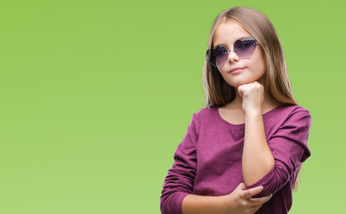 Young beautiful girl wearing sunglasses over isolated background with hand on chin thinking about question, pensive expression. Smiling with thoughtful face. Doubt concept.