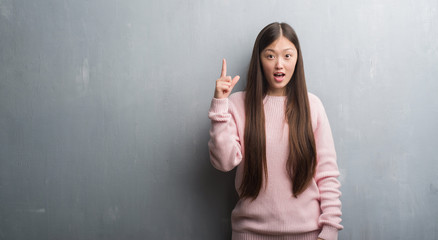 Young Chinese woman over grey wall pointing finger up with successful idea. Exited and happy. Number one.