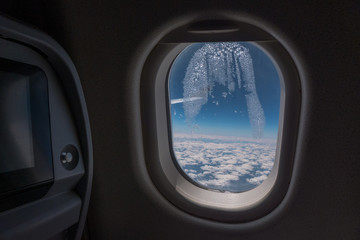 Frozen condensation in the window of an airplane with the wing in the back.