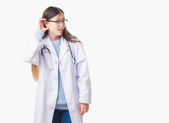Young Chinese doctor woman over isolated background smiling with hand over ear listening an hearing to rumor or gossip. Deafness concept.