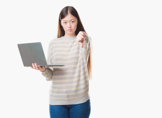 Young Chinese woman over isolated background using computer laptop with angry face, negative sign showing dislike with thumbs down, rejection concept