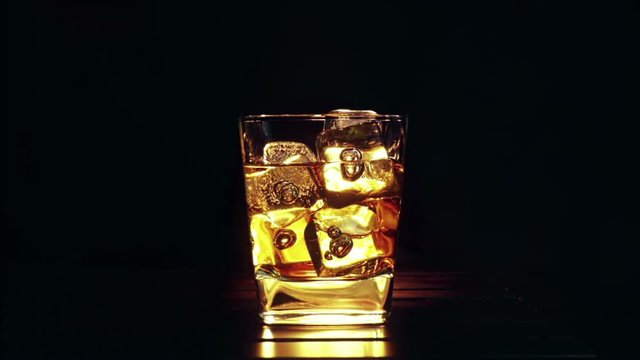 barman pouring whiskey in the glass with ice cubes on wood table and black dark background, focus on ice cubes, whisky relax time on warm atmosphere