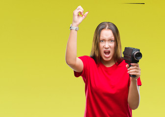 Young beautiful caucasian woman filming using vintage video camera over isolated background annoyed and frustrated shouting with anger, crazy and yelling with raised hand, anger concept