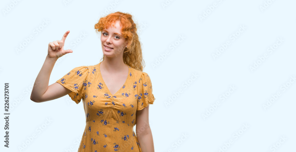 Wall mural Young redhead woman smiling and confident gesturing with hand doing size sign with fingers while looking and the camera. Measure concept.