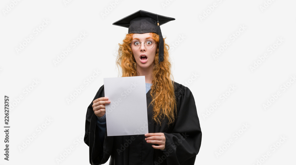 Canvas Prints young redhead woman wearing graduate uniform holding degree scared in shock with a surprise face, af