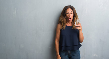 Middle age hispanic woman drinking glass of water scared in shock with a surprise face, afraid and excited with fear expression