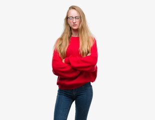 Blonde teenager woman wearing red sweater skeptic and nervous, disapproving expression on face with...