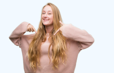 Blonde teenager woman wearing pink sweater looking confident with smile on face, pointing oneself with fingers proud and happy.