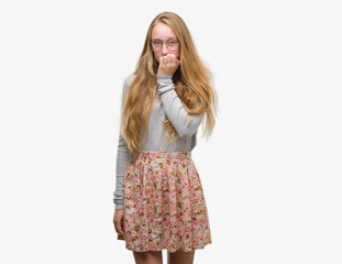 Blonde teenager woman wearing flowers skirt looking stressed and nervous with hands on mouth biting nails. Anxiety problem.