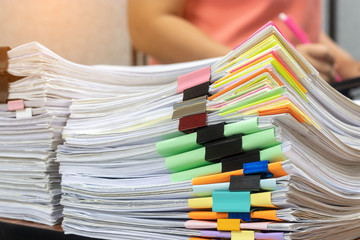 Teacher is checking student homework assignment and report on table in office for score. Unfinished paperwork stacked in archive with colorful papers and paper clips. Education and business concept.