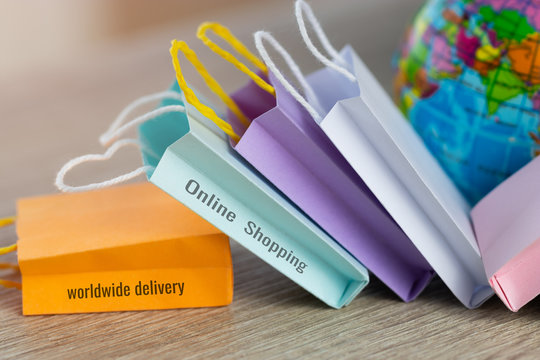 The word worldwide delivery, text on shopping paper bag, on wooden table with globe near by. Consumer can buy products directly anywhere anytime from seller. Online shopping and e-commerce concept.