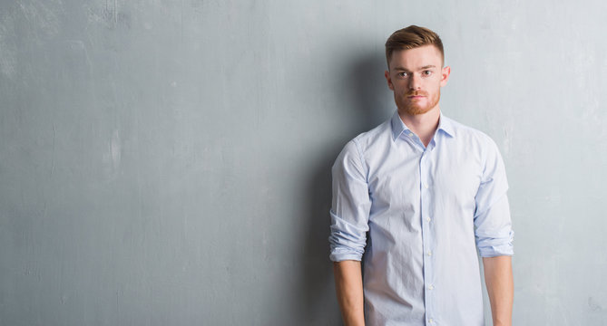 Young redhead business man over grey grunge wall with serious expression on face. Simple and natural looking at the camera.
