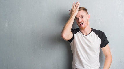Young redhead man over grey grunge wall surprised with hand on head for mistake, remember error....