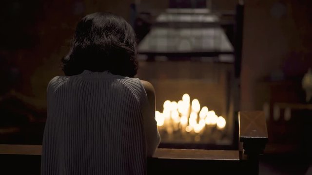 Back view of young woman praying in the church with candle light background. Shot in 4k resolution